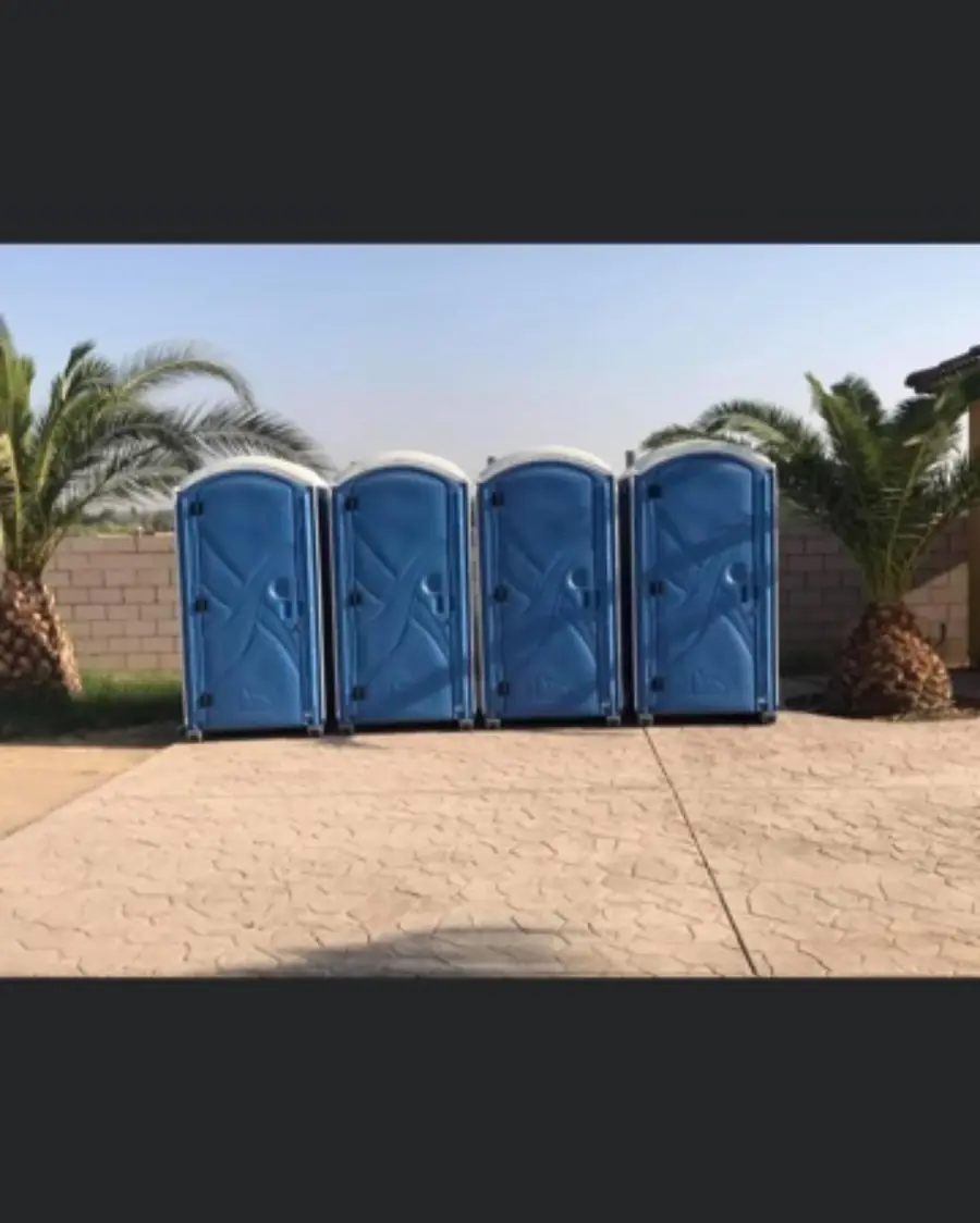 Four blue porta potties lined up on a paved lot