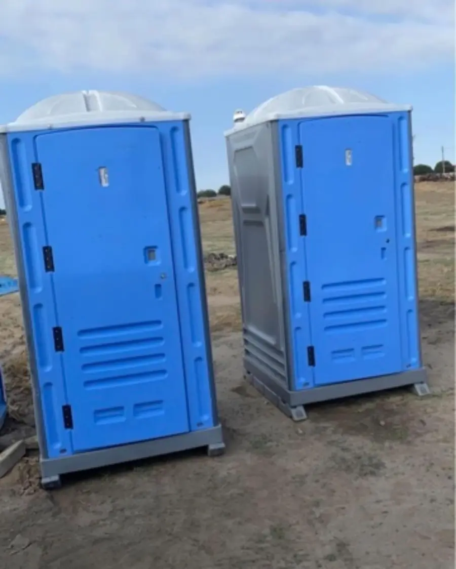 Two blue portable toilets on bare ground at a building site
